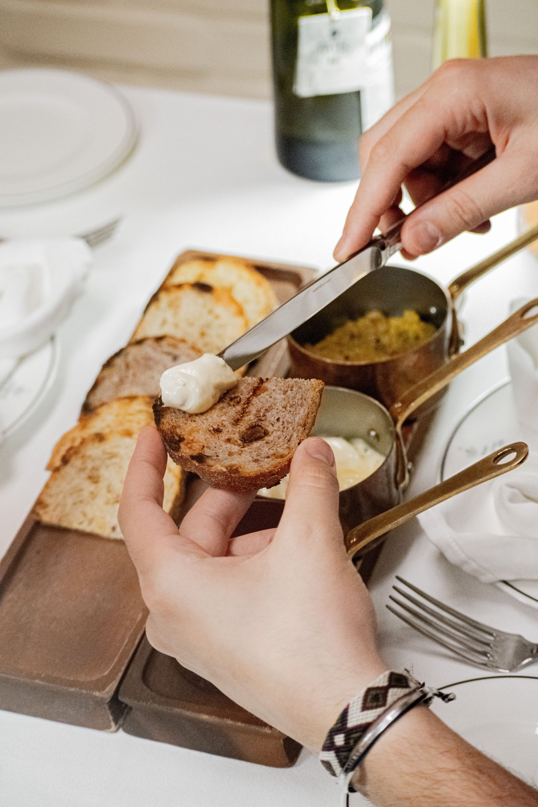 A hand spreading butter with a knife onto a slice of toasted bread over a wooden board of sliced bread